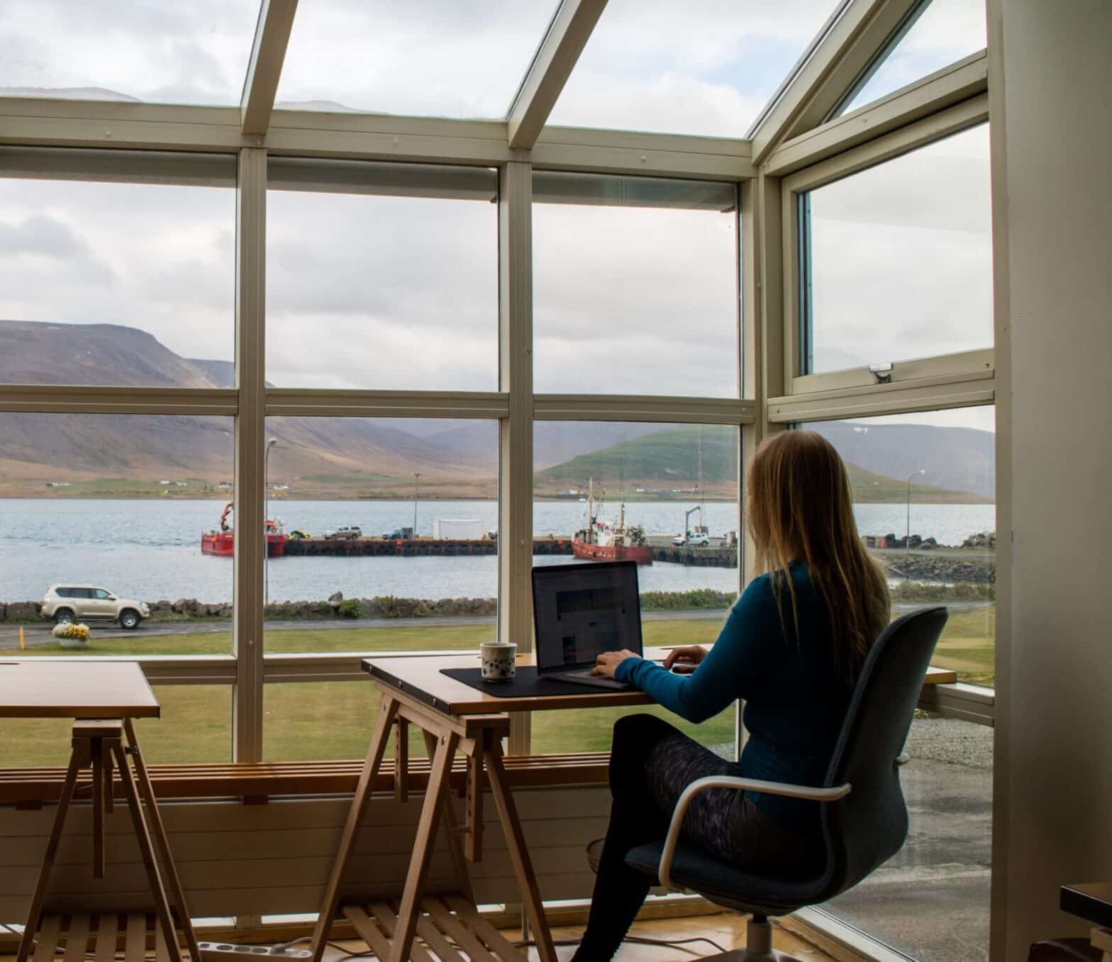 Woman sitting at her computer in her home office looking out the window at beautiful scenery.